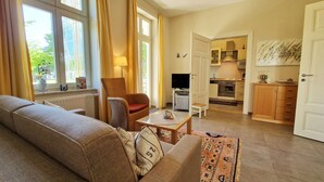 A living room with a sofa, a chair, a coffee table, and a view of the kitchen through an open door.