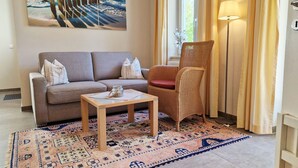 A living room with a sofa, a wicker chair, a small table, and a patterned rug.