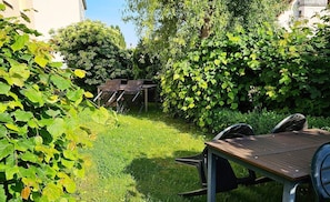 Un jardin avec une table et des chaises en bois, entourĂ© dâune vĂ©gĂ©tation luxuriante et dâarbres.