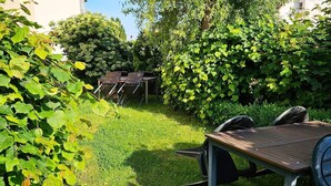 Un giardino con tavolo e sedie di legno, immerso nel verde e alberi.