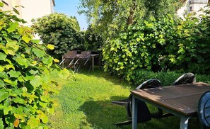 Un jardin avec une table et des chaises en bois, entourĂ© dâune vĂ©gĂ©tation luxuriante et dâarbres.