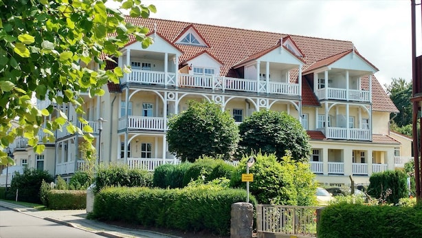 Un hotel de varios pisos con balcones, techo de tejas rojas y jardines bien cuidados.