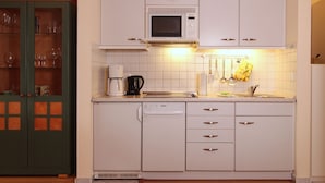 Cocina pequeña con armarios blancos, microondas, lavavajillas y cafetera.