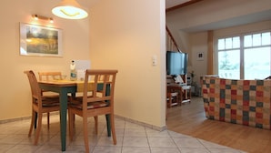 Un área de comedor con una mesa y sillas, un televisor al fondo y vistas al exterior a través de ventanas amplias.