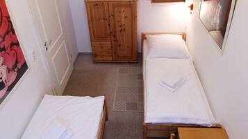 Ein kleines, schmales Zimmer mit zwei Einzelbetten, einem Holzschrank und einem kleinen Tisch.