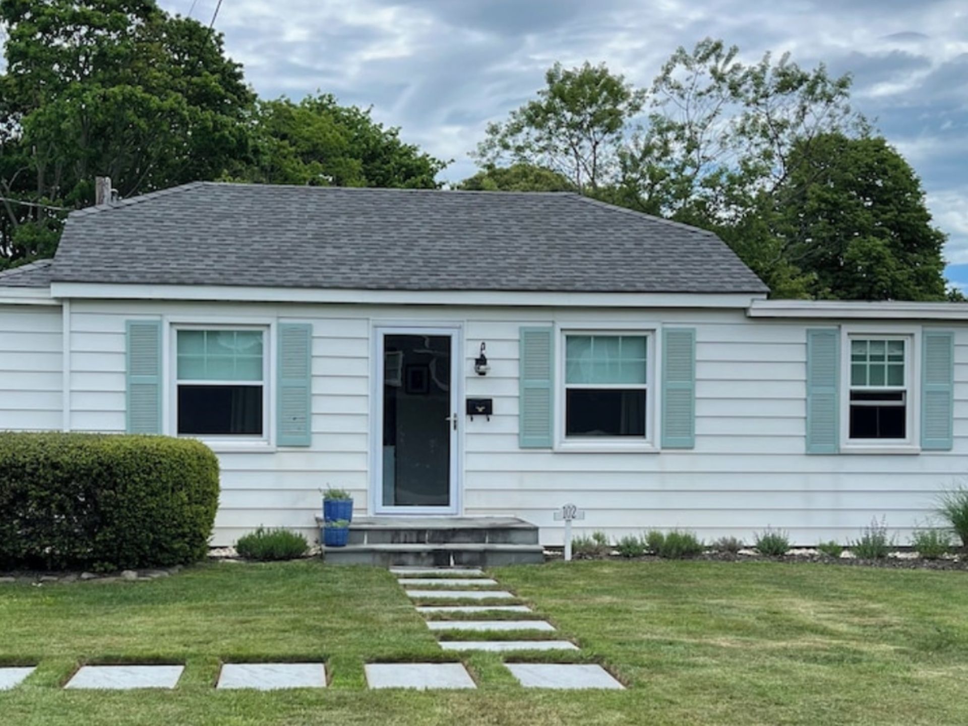 A single-story house with a front door, two windows with shutters, and a small porch.