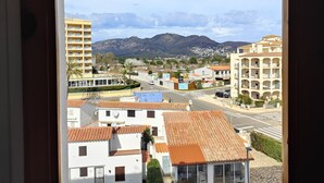 Vista desde una ventana de un edificio con tejado de tejas, una calle con coches y montañas al fondo.