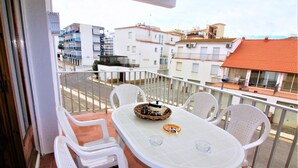 Uma varanda com mesa e cadeiras, vista para a rua e edifícios ao fundo.