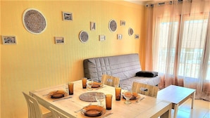 Uma sala de jantar com mesa posta para quatro pessoas, um sofá e uma janela com cortinas.