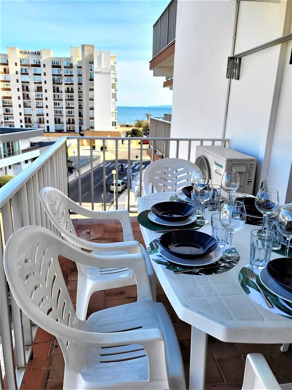 A balcony table set with plates, glasses, and cutlery, overlooking a street and buildings.