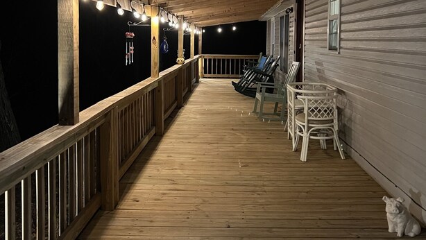 Una terraza de madera con luces colgantes, barandilla y un perro blanco.