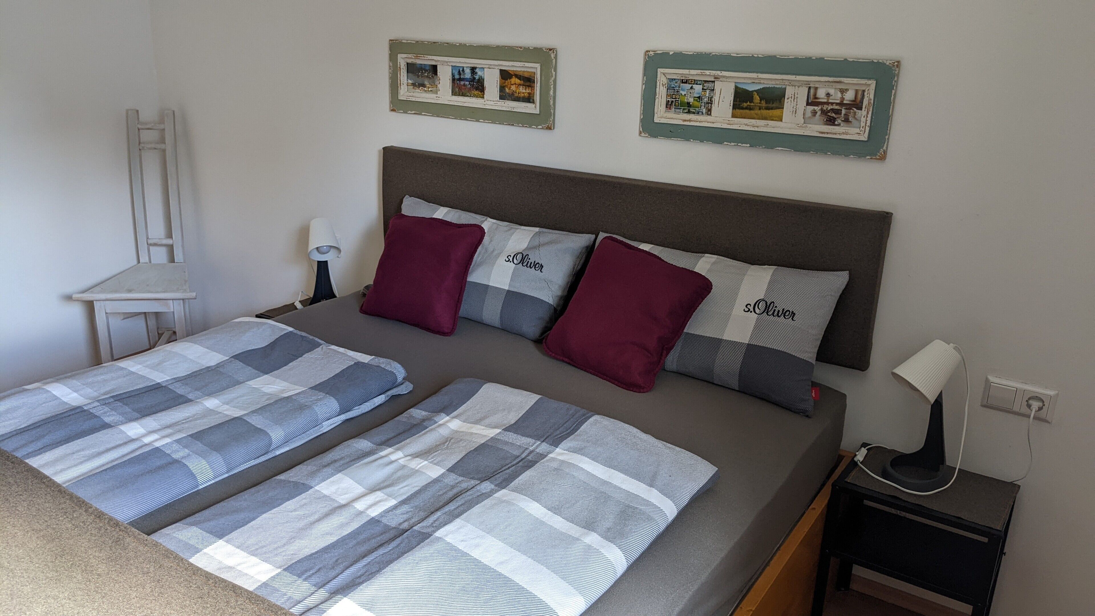 Ein Doppelbett mit zwei Kissen, ein Nachttisch, eine Lampe und zwei gerahmte Bilder an der Wand.