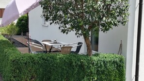 Um pátio com uma mesa, cadeiras, uma árvore e um arbusto.