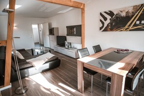 Um espaço de estar moderno com uma mesa de jantar, sofá e uma televisão ao fundo.