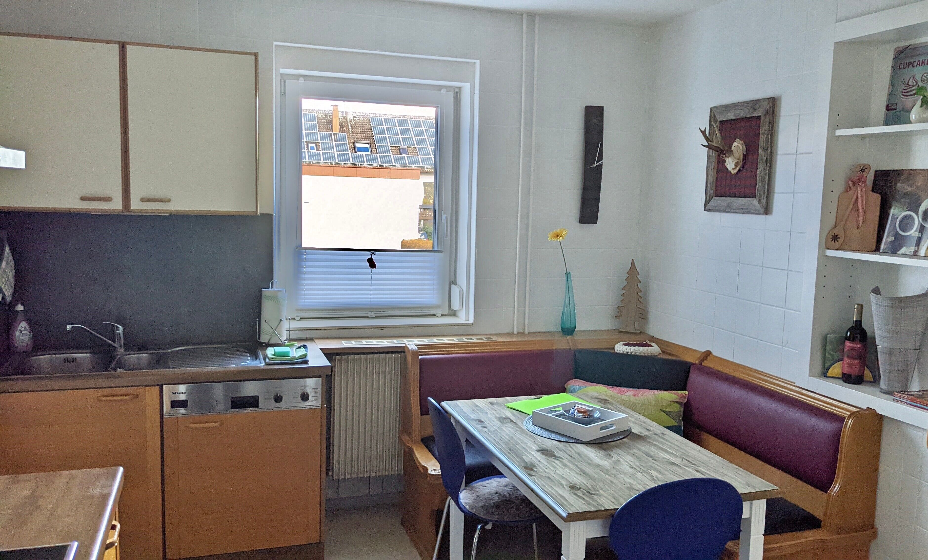 Une cuisine compacte avec une fenêtre, un radiateur, un évier et un coin repas comprenant un banc et une table.