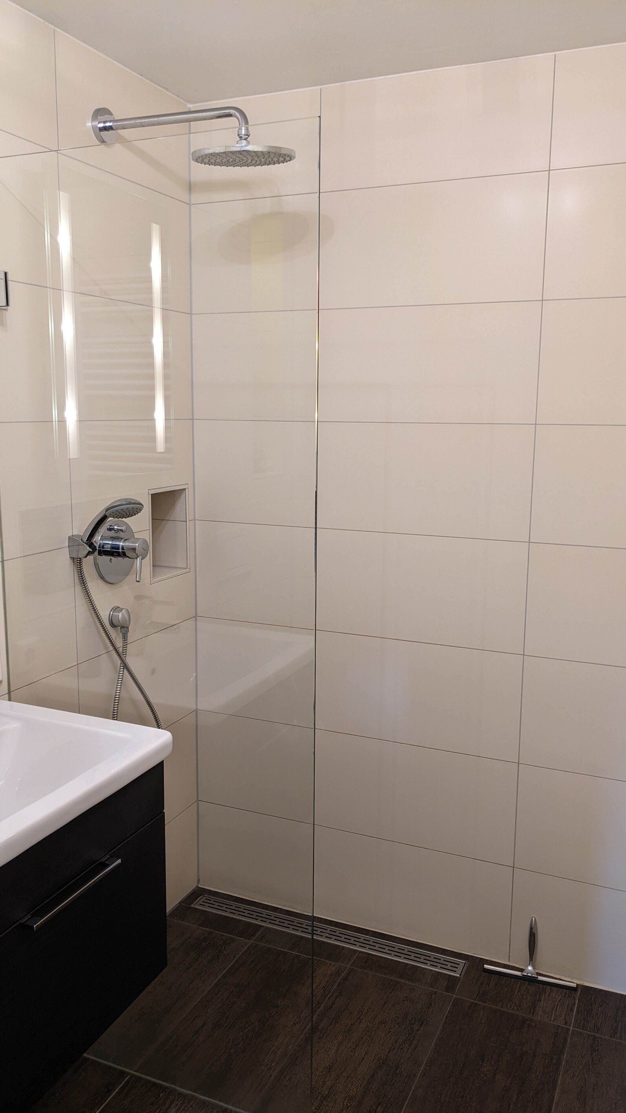 A bathroom with a shower, a sink, and a dark wooden floor.