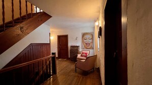 Un escalier en bois mène à une pièce dotée d’un plancher en bois, d’une porte, d’une chaise et d’un luminaire fixé au mur.
