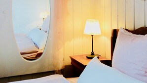 Une chambre à coucher avec un lit, une table de chevet avec une lampe, un miroir et une fenêtre.