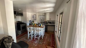 Cocina compacta con armarios blancos, microondas, estufa y comedor con sillas blancas.