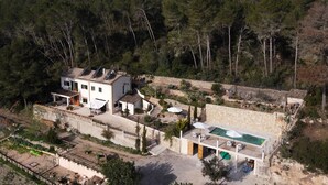 Una villa bianca con piscina, immersa tra alberi e circondata da un muro in pietra.