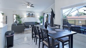 A modern living room with a dining area, a ceiling fan, and a large window with a view. - The Modern/Luxe Vacation • Heated Pool •  Disney (Davenport)