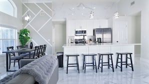 A modern kitchen with white cabinets, a central island with stools, a dining area with a table and chairs, and a large window. - The Modern/Luxe Vacation • Heated Pool •  Disney (Davenport)