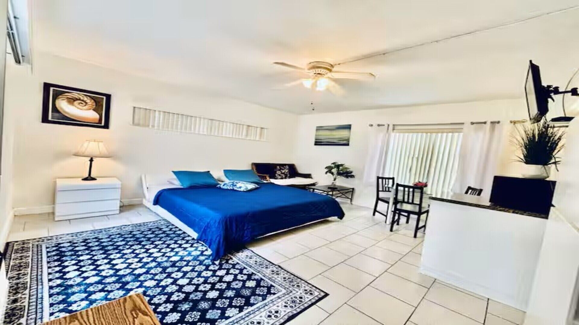 A bedroom with a bed, a nightstand, a desk, a chair, and a ceiling fan.