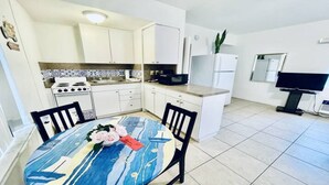 A compact kitchen with white cabinets, a stove, a microwave, and a refrigerator. There's a dining table with chairs and a bouquet of flowers. - Beach Tide Motel - #6 Studio 1 King bed (Hollywood)