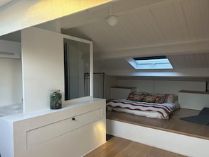 A compact bedroom with a skylight, a bed with floral bedding, a bedside table, and a small cabinet.