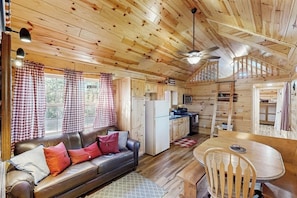 A cabin interior with a sofa, dining table, kitchen area, and a staircase.