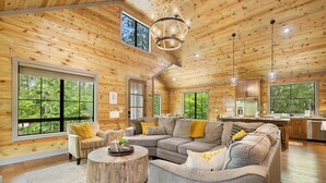 A spacious cabin interior with a large living area, a kitchen, and multiple windows offering views of the forest. - Beyond Pines. Family-Friendly Escape & Retreat (Broken Bow)