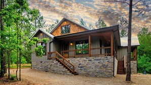 A modern log cabin with a stone foundation, a wooden deck, and a staircase leading to the entrance. - Beyond Pines. Family-Friendly Escape & Retreat (Broken Bow)