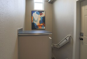 A hallway with a white door, a small window, and a piece of abstract art on a shelf.