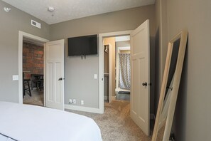 A bedroom with a bed, a TV mounted on the wall, and a door leading to a bathroom.