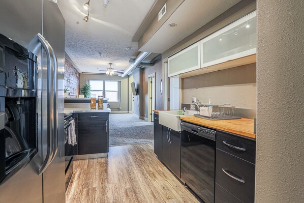 A modern kitchen with dark cabinetry, a wooden countertop, and a built-in dishwasher.