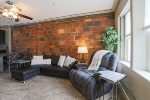 A living room with a brick wall, a sectional sofa, a small table, and a potted plant.