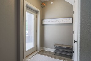 A hallway with a door, a bench, and a sign that reads "COME IN AND Stay Awhile".