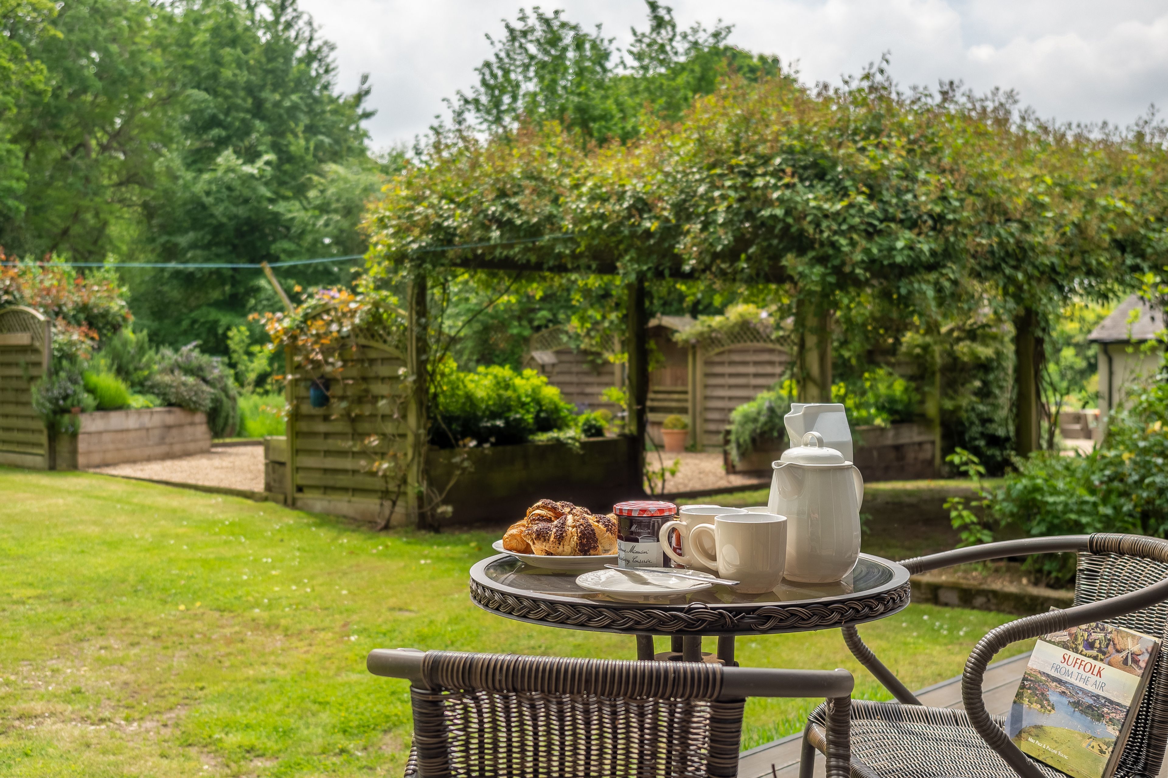 A wicker table with a tea set and pastries in a garden setting.