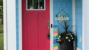 Una casa blu vivace con una porta rossa brillante, un cartello di benvenuto e una pianta in vaso.