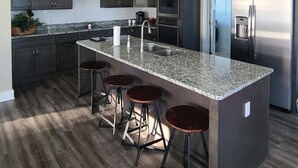 Una cucina moderna con mobili scuri, un piano di lavoro in granito, elettrodomestici in acciaio inossidabile e un'isola centrale con sgabelli da bar.