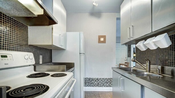 A compact kitchen with a white stove, stainless steel sink, and cabinets. - Warm apartment with a bus stop at its doorstep (Montreal)