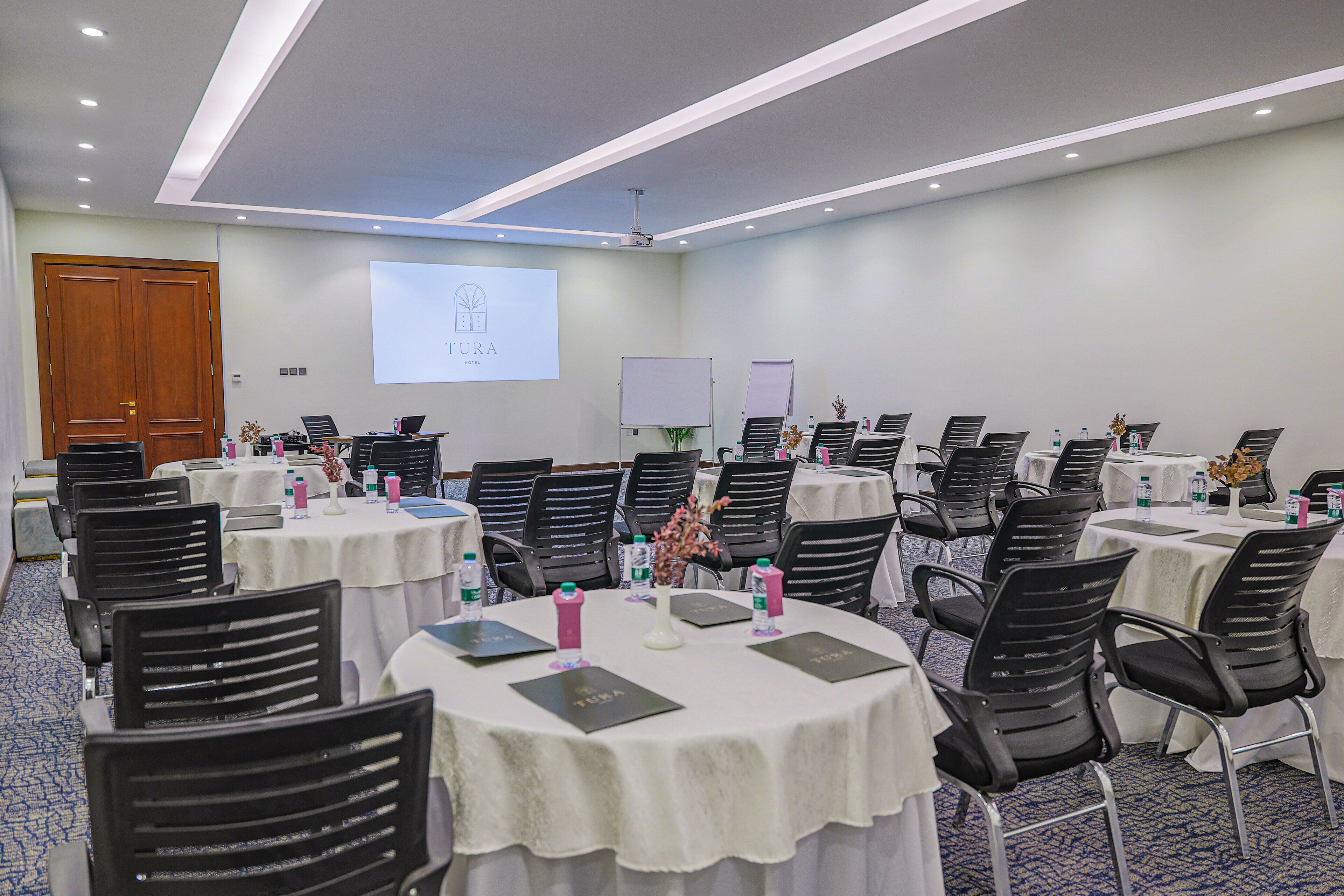 A conference room with multiple tables, chairs, and a presentation screen.