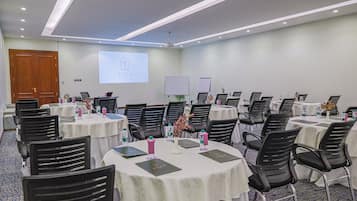 A conference room with multiple tables, chairs, and a presentation screen.