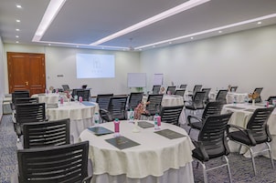 A conference room with multiple tables, chairs, and a presentation screen.