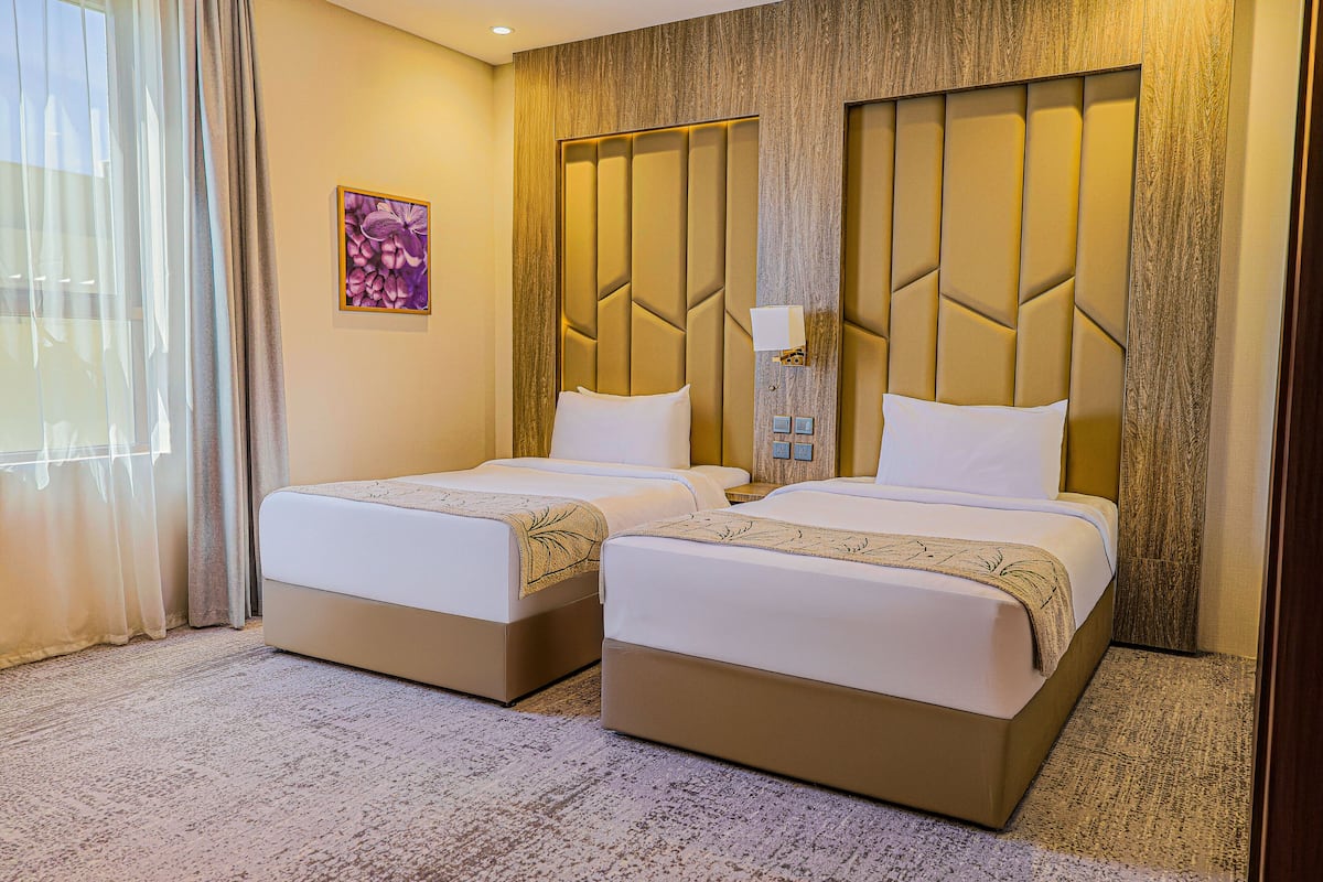 Habitación de hotel con dos camas, un ventanal grande con cortinas, un cabecero de madera y una lámpara fijada a la pared.