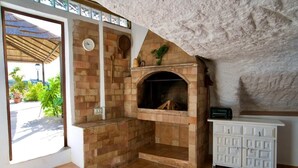 A stone fireplace with a clock, a white cabinet, and a view of greenery outside.
