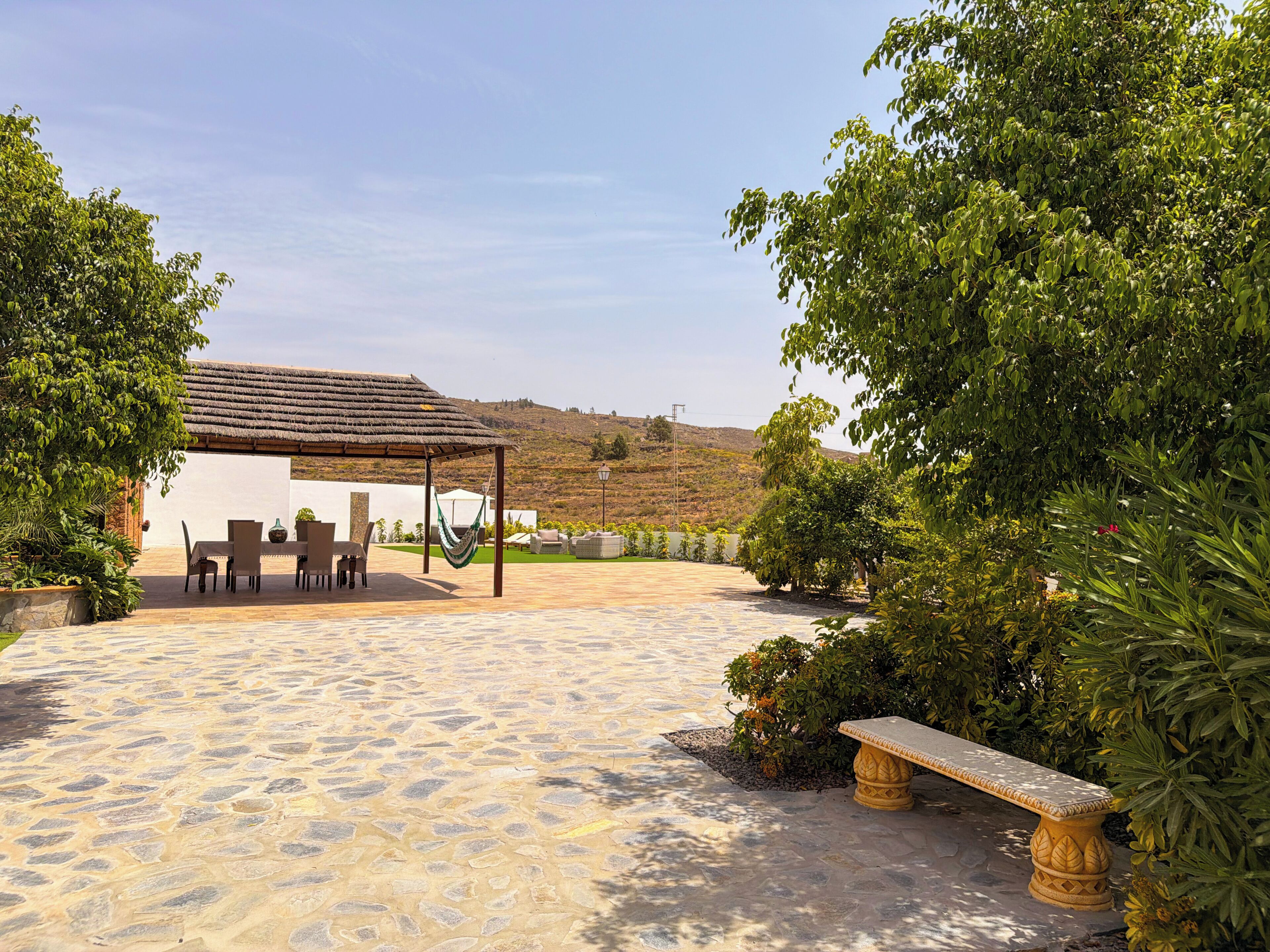 Un patio con piso de piedra, una mesa con sillas, una hamaca y un banco.