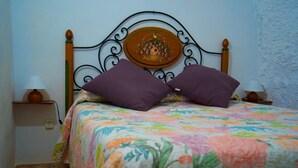 A bed with a floral bedspread, two purple pillows, and a decorative plate on the headboard.