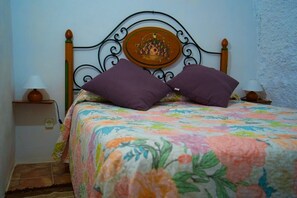 Un lit avec une couvre-lit à motifs floraux, deux oreillers violets et une assiette décorative posée sur la tête de lit.