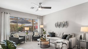 Una sala de estar moderna con un sofá gris, dos sillones, una mesa de centro y un ventilador de techo.